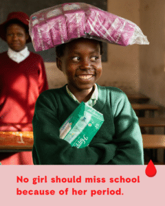A smiling schoolgirl standing in a classroom, proudly holding menstrual pads — representing access to period products and the power of education.