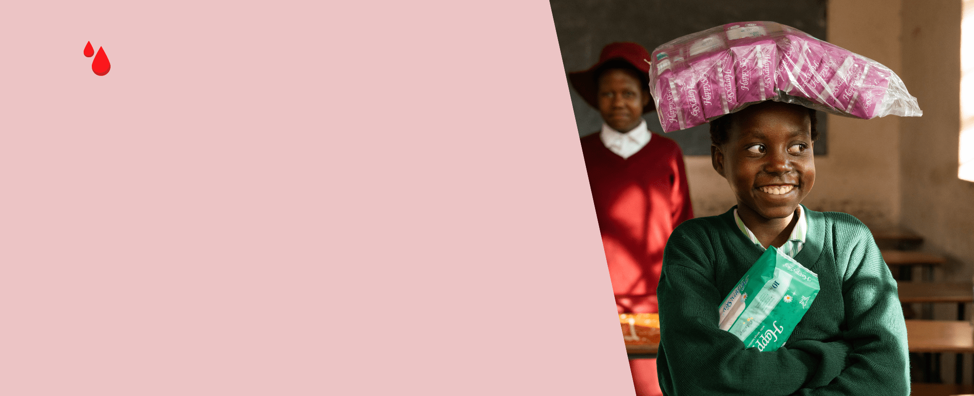 A smiling schoolgirl standing in a classroom, proudly holding menstrual pads — representing access to period products and the power of education.