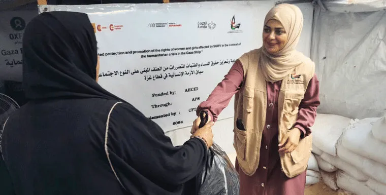 Women distributing aid packages at a humanitarian event, supported by international organizations, in a tented area.